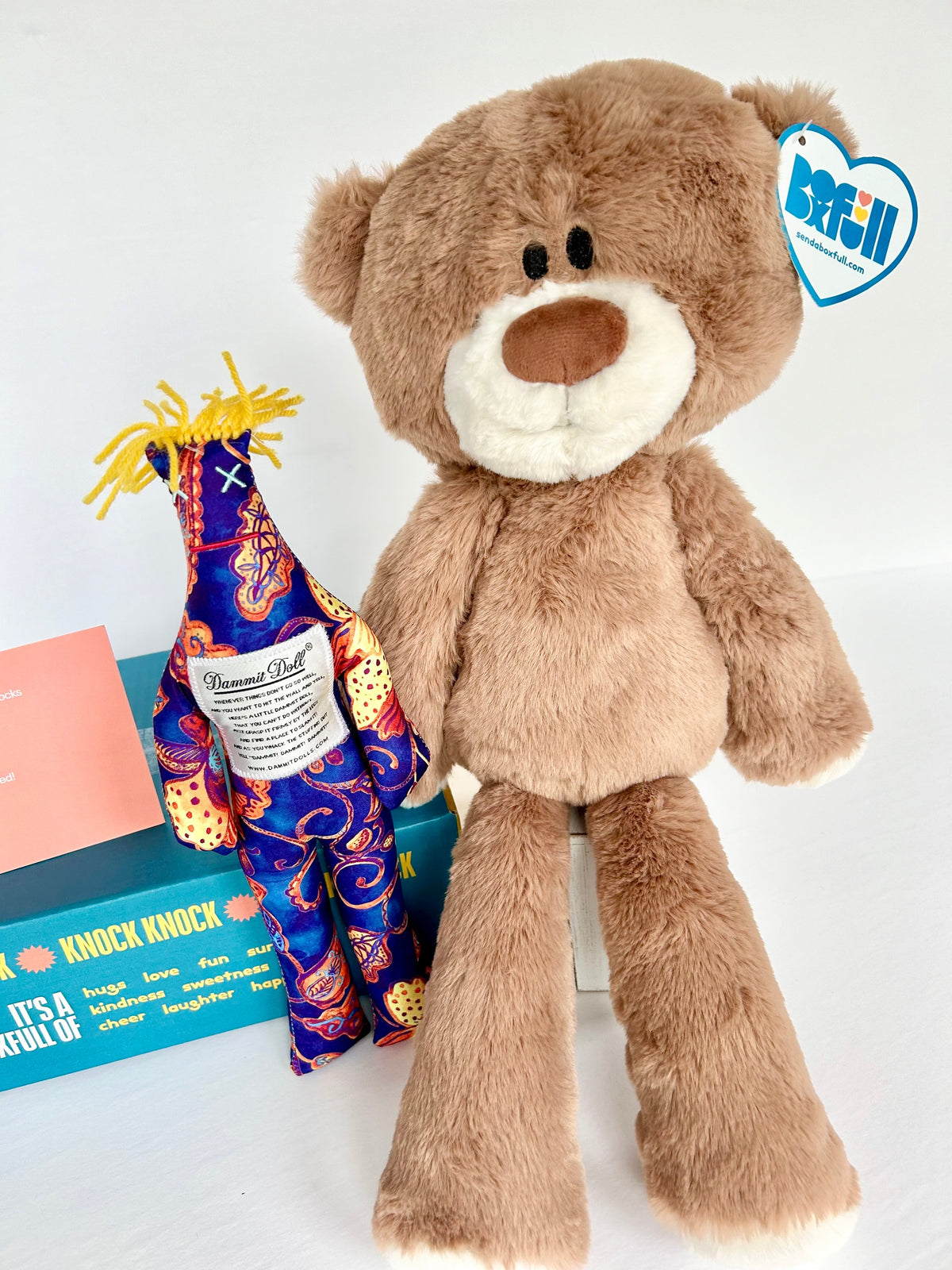 22in Teddy Bear next to a colorful dammit doll.